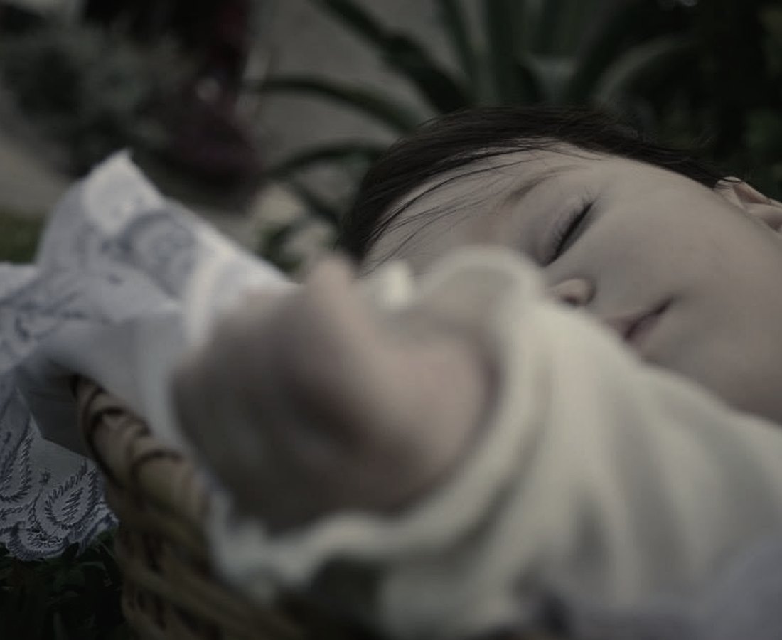 A sleeping baby resting in a wicker basket outdoors