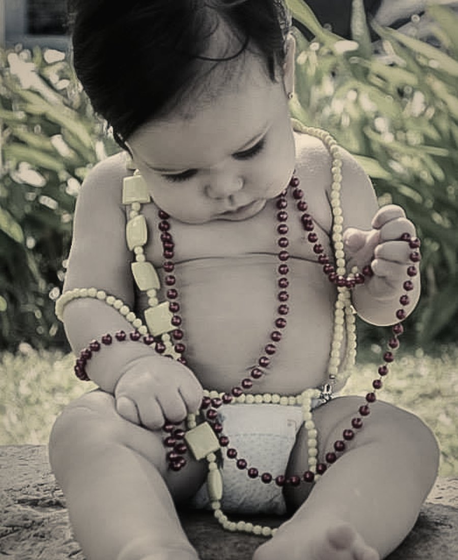 A baby playing with strands of beads in the garden