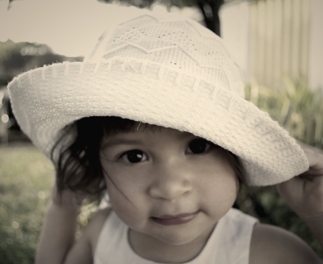 A little girl holding the brim of a white sun hat in the garden